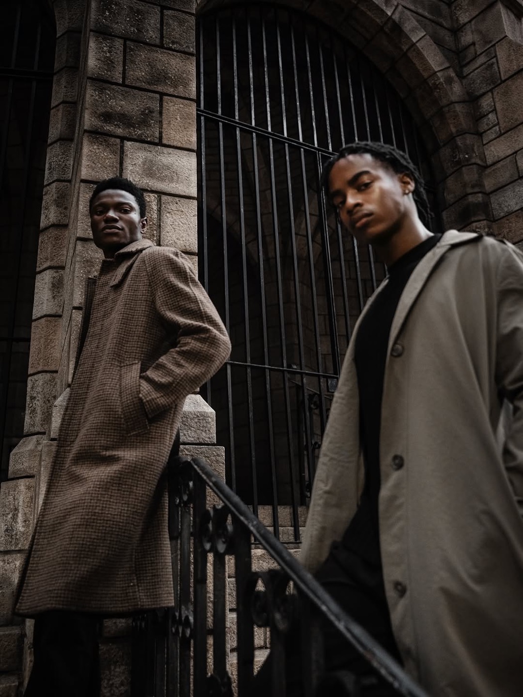 Editorial portrait of two men in coats against stone architecture